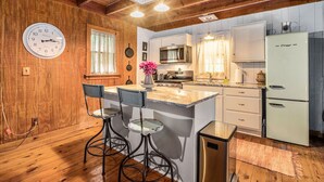 Una cocina con paredes de madera, una isla central con taburetes de bar, un reloj y electrodomésticos modernos.