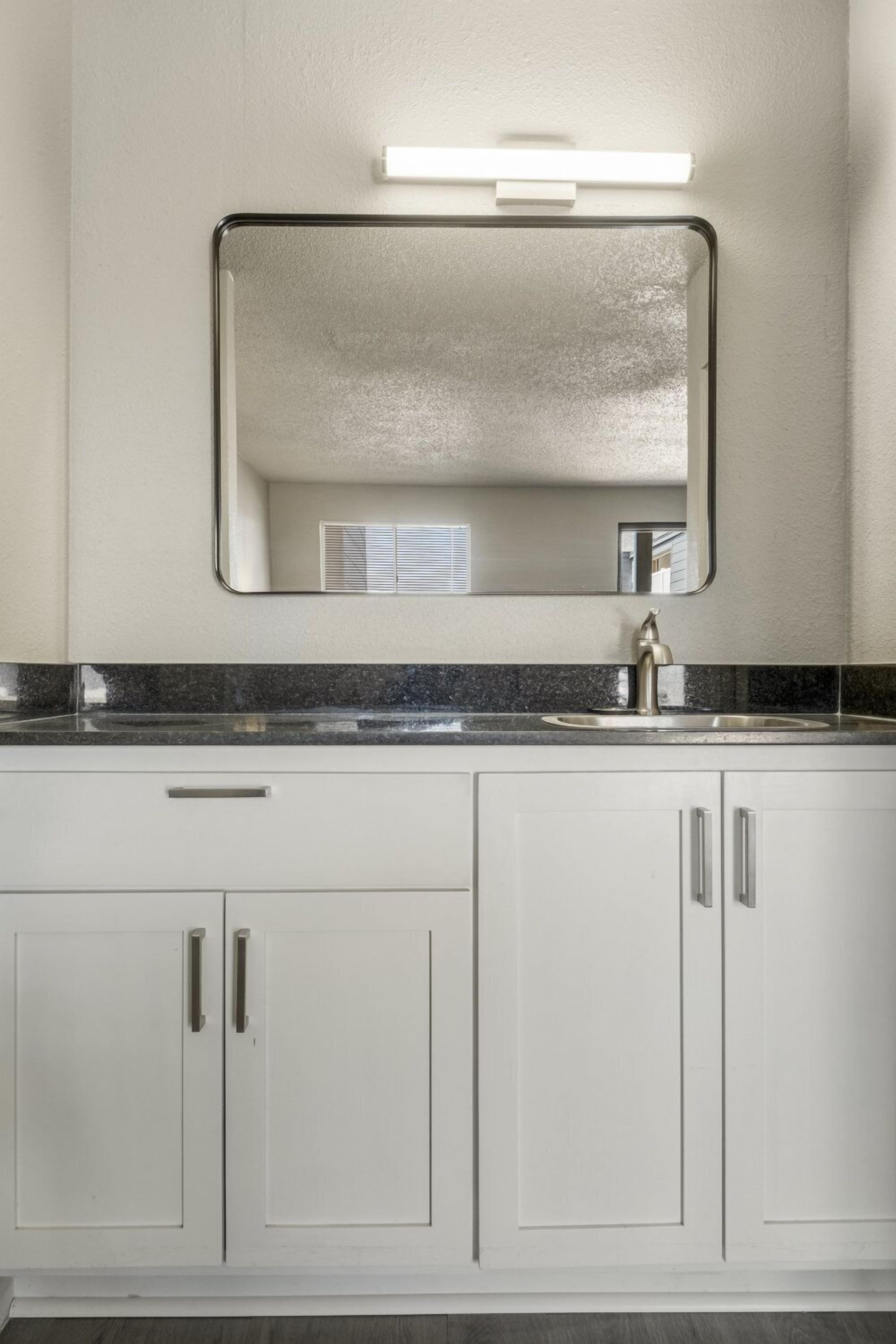 A bathroom with a white vanity, a sink, and a mirror.