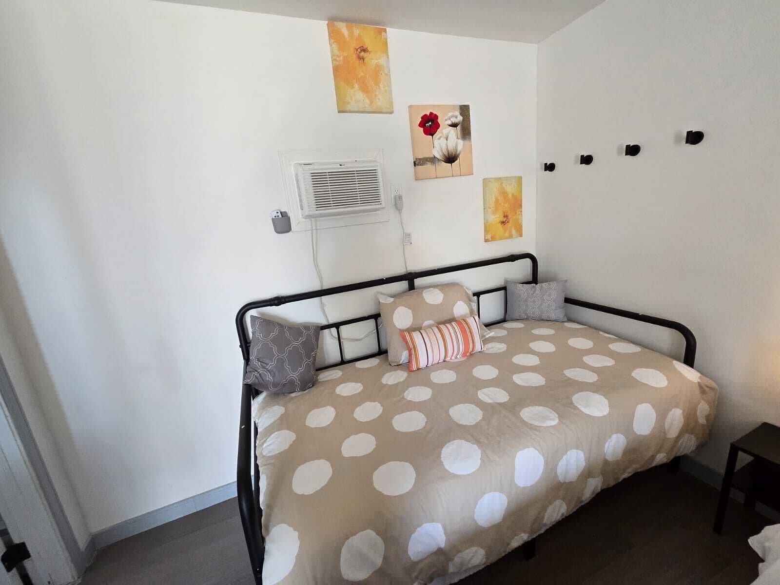A bedroom with a bed, a wall-mounted air conditioner, and three paintings.