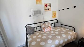 A bedroom with a bed, a wall-mounted air conditioner, and three paintings.