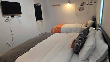 A hotel room with two beds, a TV, a wall-mounted light, and a painting.