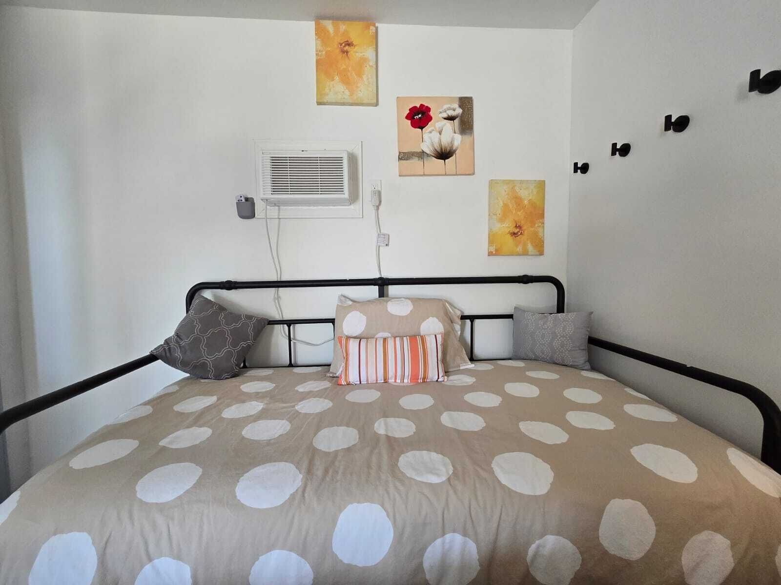 A bedroom with a bed, a wall-mounted air conditioner, and three paintings.