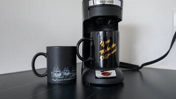Uma cafeteira preta e uma caneca preta com o desenho de um barco e texto sobre uma mesa.