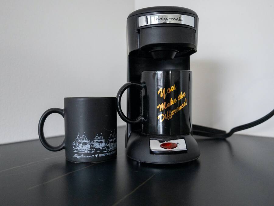 Uma cafeteira preta e uma caneca preta com o desenho de um barco e texto sobre uma mesa.