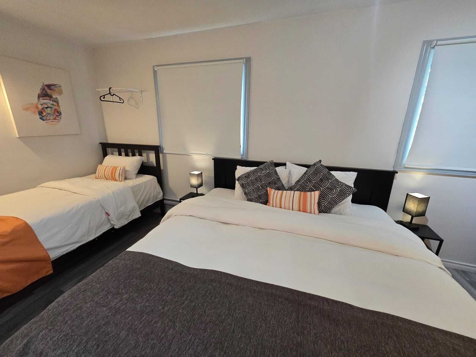 A hotel room with two single beds, a large bed, and a nightstand with a lamp.