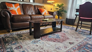 A living room with a brown leather sofa, a wooden coffee table, and a patterned rug.