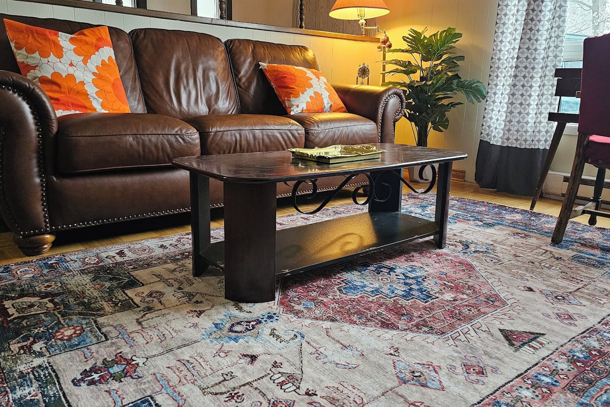 A living room with a brown leather sofa, a wooden coffee table, and a patterned rug.