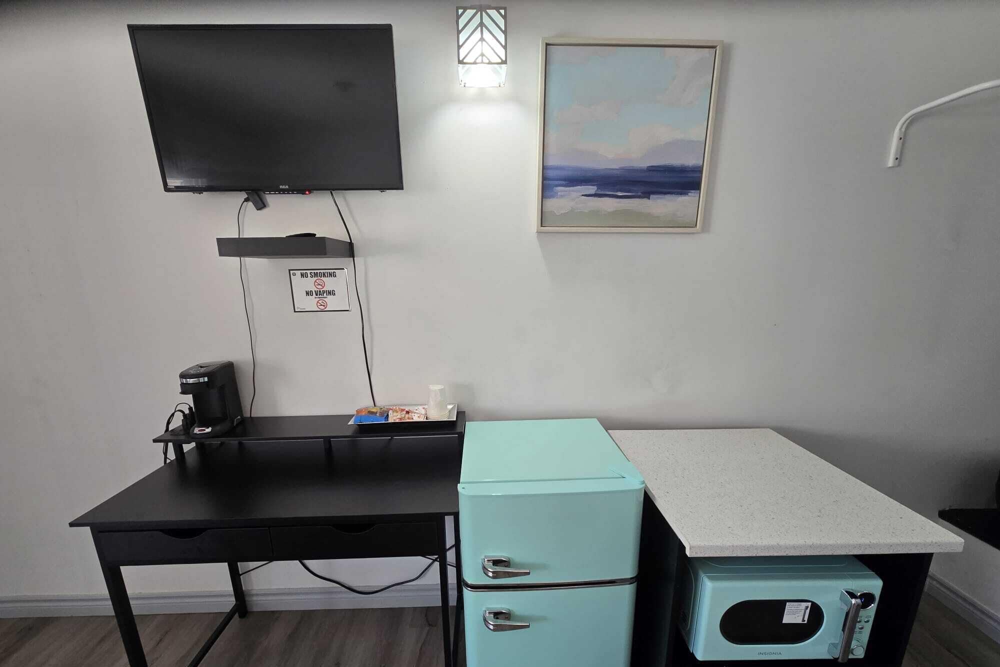 Une chambre dotée d’un téléviseur à écran plat fixé au mur, d’un panneau « Il est interdit de fumer », d’un tableau représentant un paysage et d’un coin cuisine équipé d’un four à micro-ondes et d’un petit réfrigérateur.