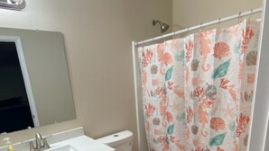 A bathroom with a white sink, a toilet, and a shower curtain with a floral pattern. There are two orange rugs on the floor.