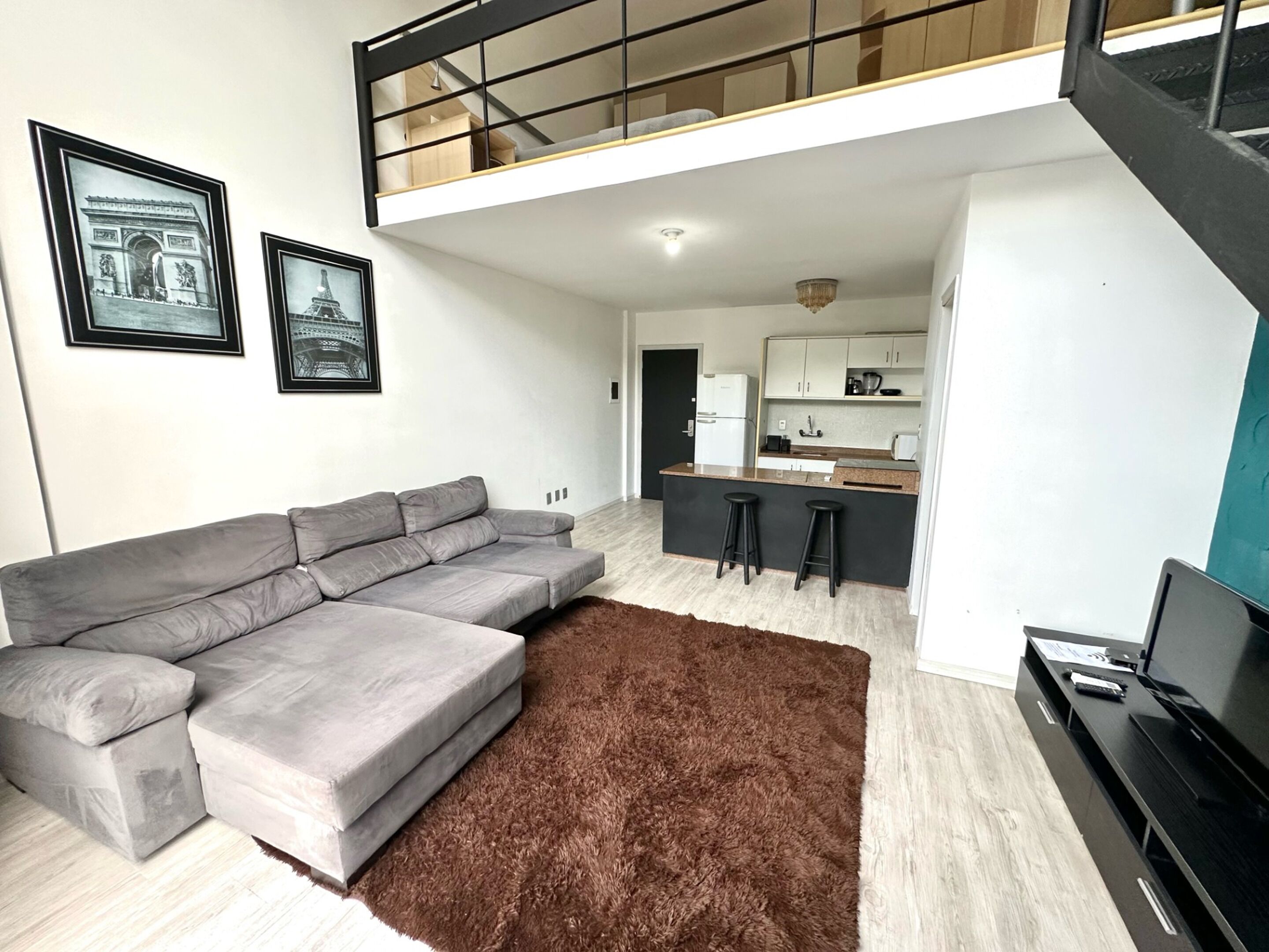 Una sala de estar moderna con un sofá seccional gris, un tapete marrón y una cocina al fondo.
