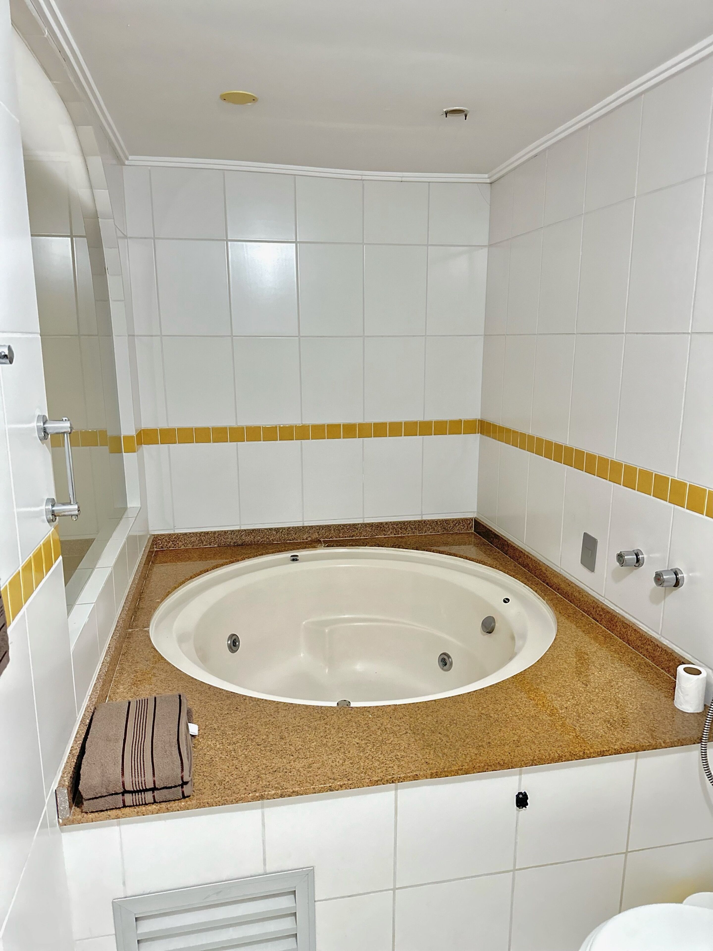 Un baño con bañera, azulejos blancos, encimera marrón y una toalla.