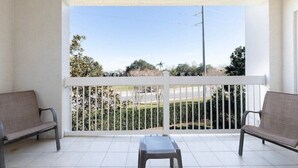 A balcony with two chairs and a small table, offering a view of a road and greenery. - Disney themed 3br condo (Kissimmee)