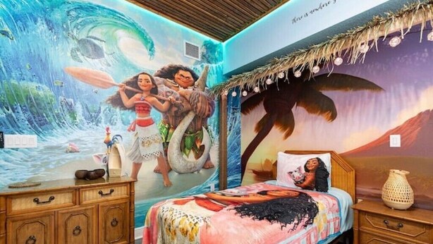 A bedroom with a mural of a tropical scene, wooden furniture, and a bed with a colorful blanket. - Disney themed 3br condo (Kissimmee)