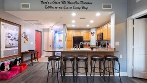 A modern kitchen with a bar area, wooden cabinets, and a large island with bar stools. - Disney themed 3br condo (Kissimmee)