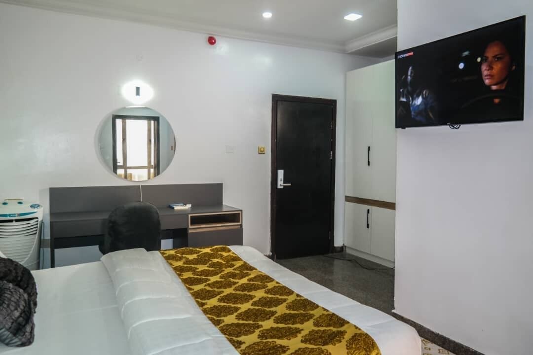 A hotel room with a bed, a desk, a chair, a wardrobe, a television, and a mirror.