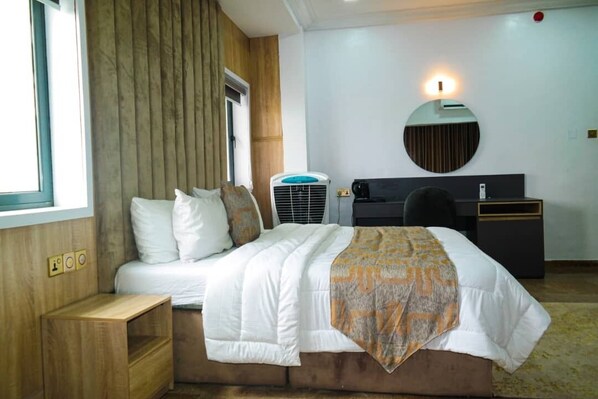 A hotel room with a bed, bedside table, desk, chair, and a round mirror. - Blue Moon Beach Hotel and Resort Lekki Lagos (Lagos)