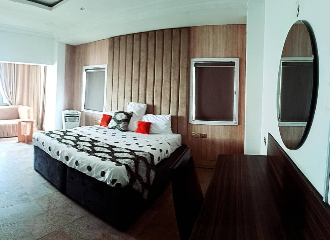 A modern bedroom with a curved headboard, a large bed with a patterned bedspread, two bedside tables, and a large mirror on the wall.
