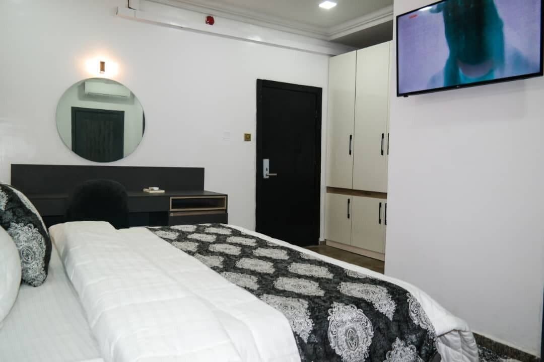 A bedroom with a bed, a desk, a chair, a wardrobe, a television, and a mirror.