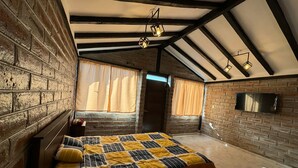 A bedroom with exposed brick walls, a bed with a striped bedspread, and a flat-screen TV mounted on the wall.