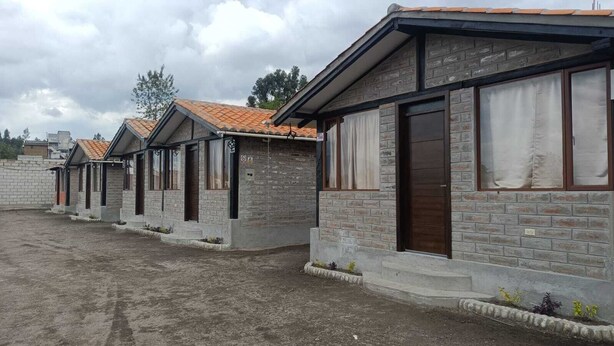 A row of small, stone-clad buildings with tiled roofs, likely guest houses or cottages, arranged in a linear fashion with a dirt ground in front.