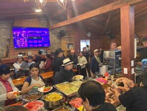 Un buffet proposant une variété de plats, avec du personnel servant et des clients se servant et mangeant.