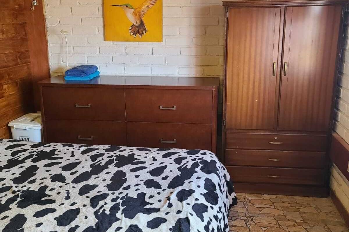 A bedroom with a bed, wooden wardrobe, and a painting on the wall.