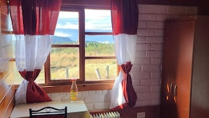 A cozy room with a wooden table, a chair, a radiator, and a window with curtains.