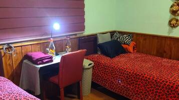 Een kamer met twee bedden, een klein tafeltje met een lamp, een stoel en een wandplank met decoratieve objecten.