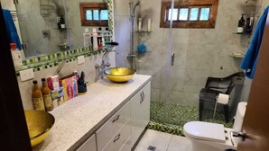 A bathroom with a large bowl sink, a toilet, and a shower area.