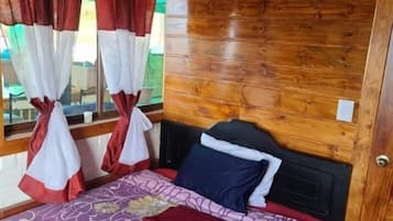 A wooden-paneled room with a bed, curtains, and a window.