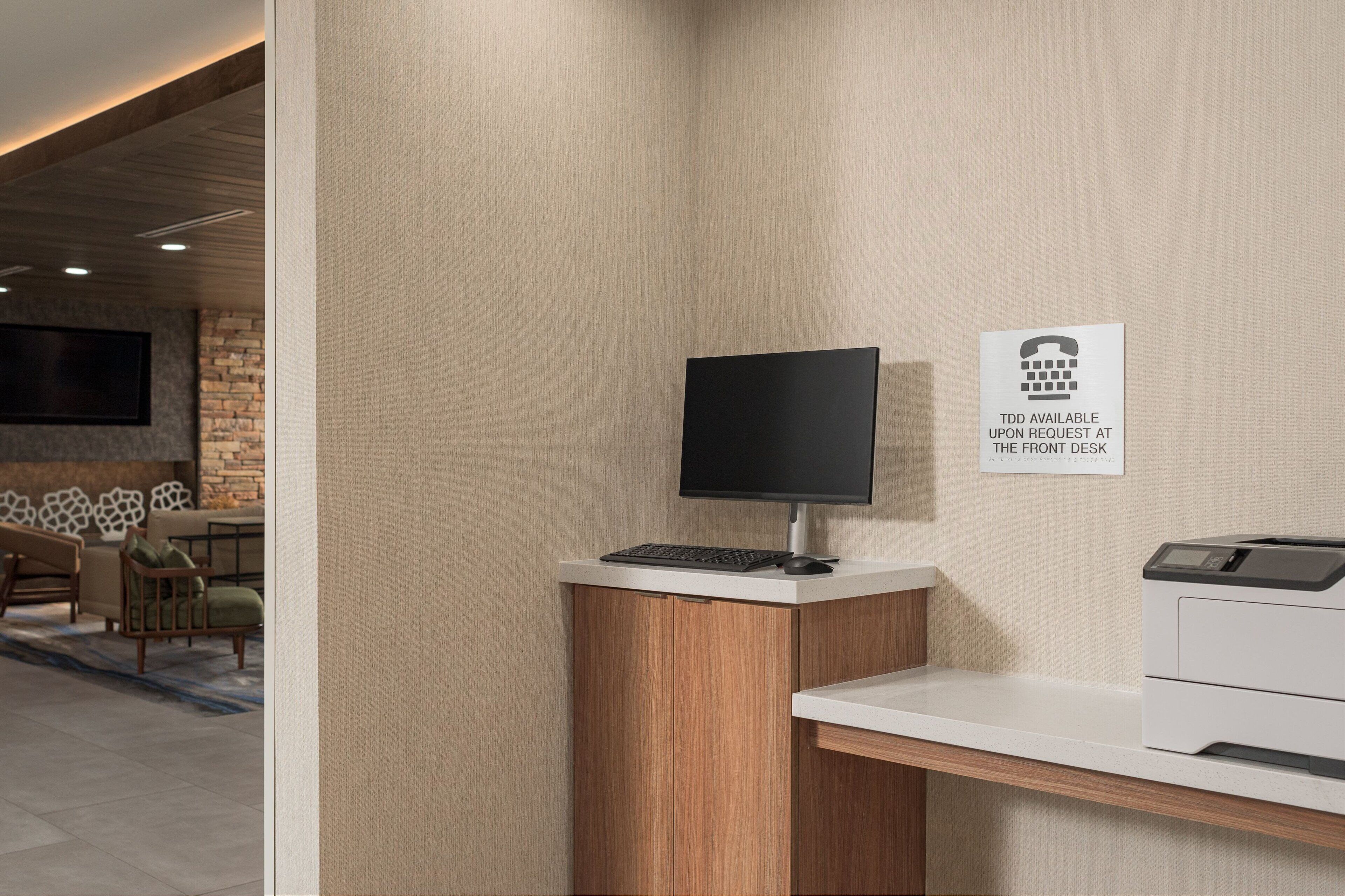 A modern reception desk with a flat-screen monitor, a keyboard, and a printer. A sign indicates that a phone is available at the front desk.