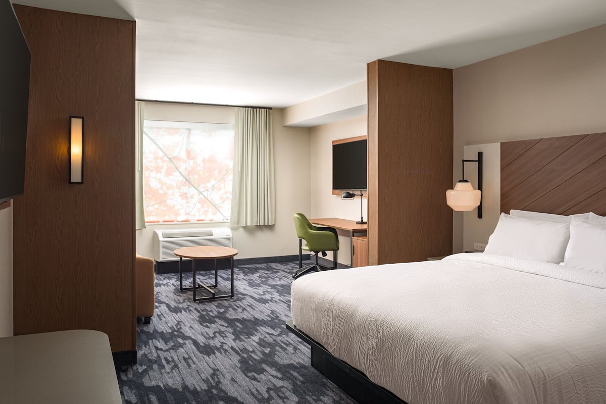 A hotel room with a large bed, a desk, a chair, and a television.