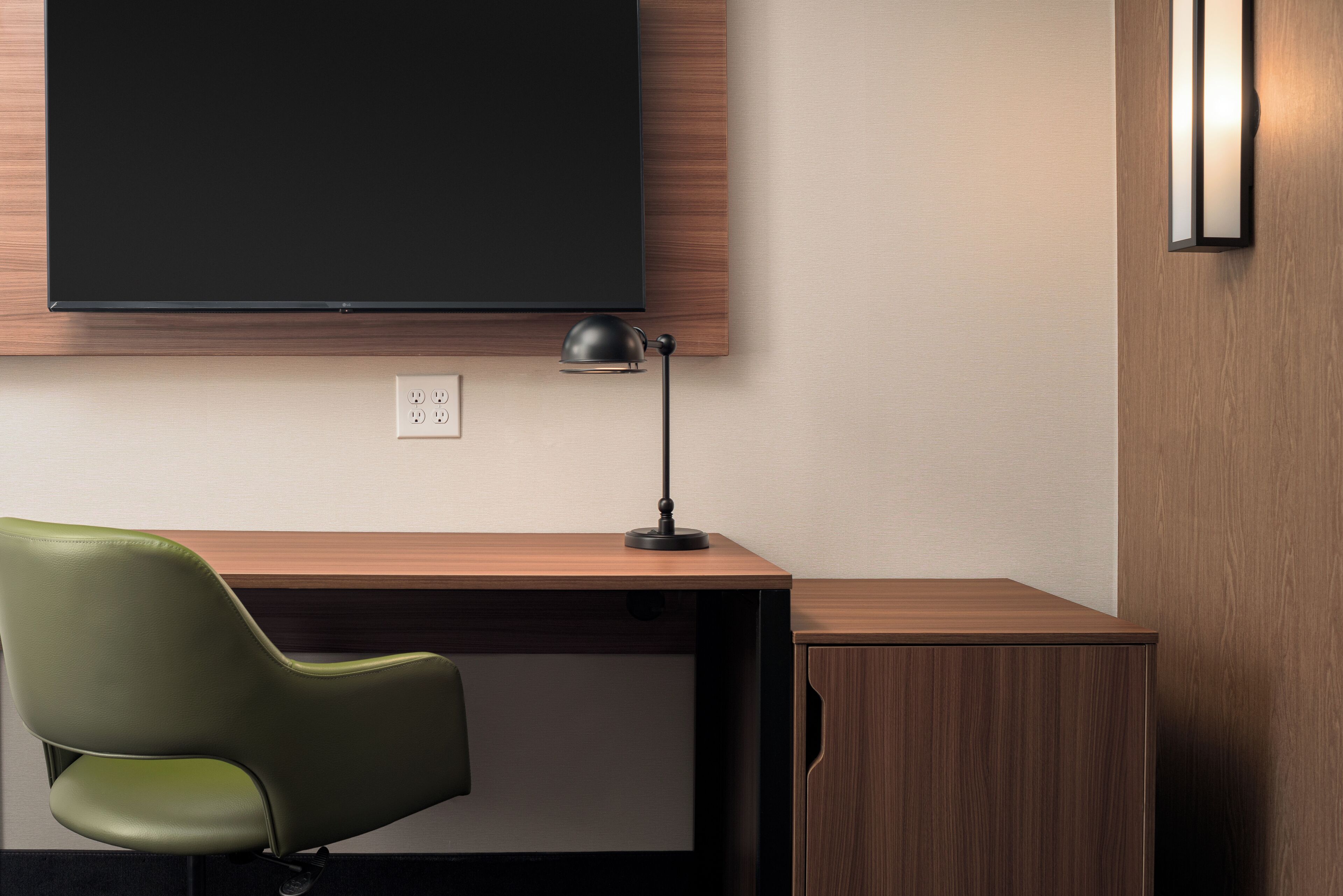 A modern office desk with a green chair, a black desk lamp, and a mounted flat-screen TV.