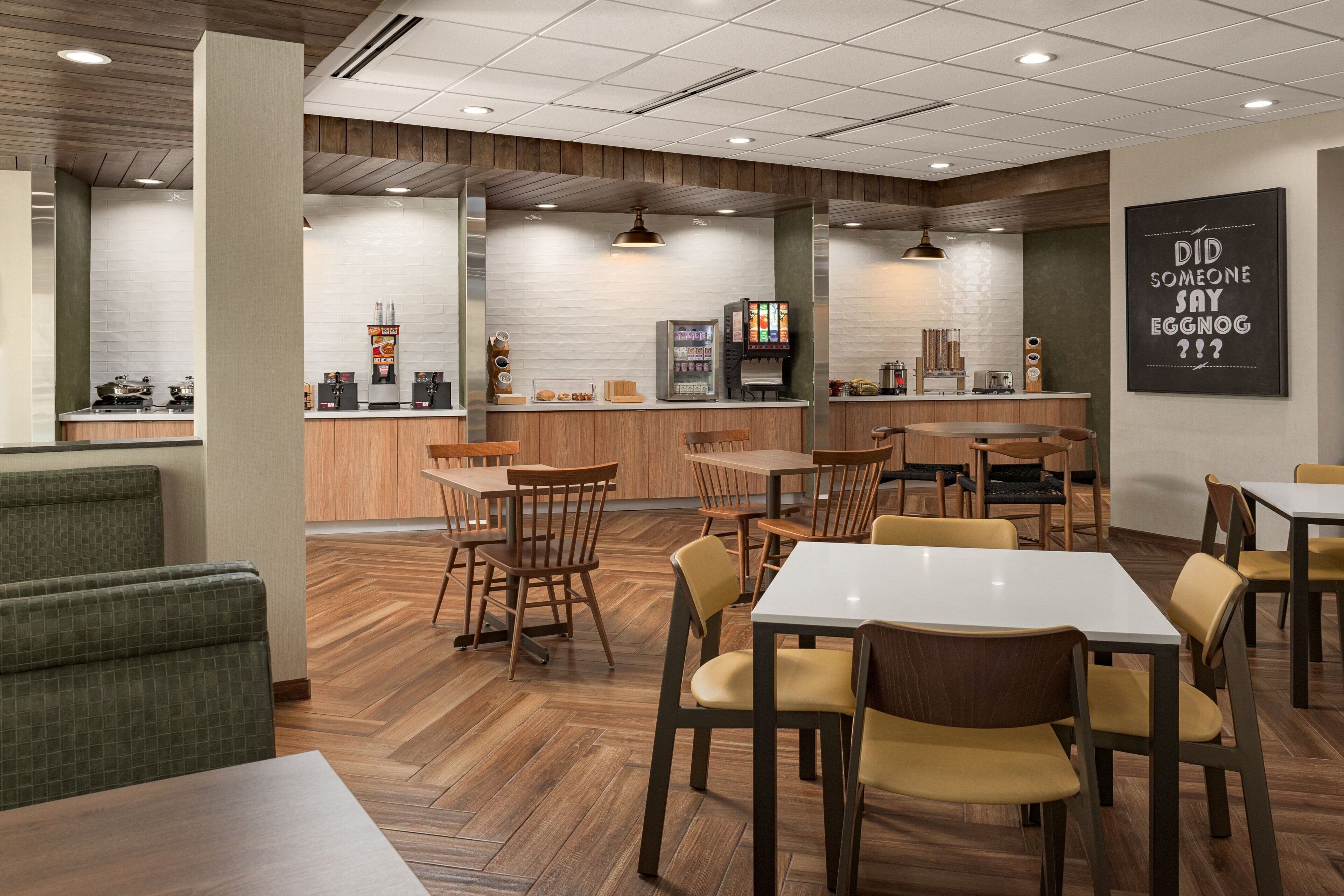 A modern cafe with wooden furniture, a counter with a coffee machine, and a wall with a humorous sign.