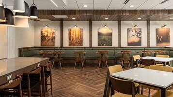 Un restaurant doté d’un parquet en bois à motifs chevrons, de banquettes confortables recouvertes d’un tissu vert, de tables et de chaises en bois, ainsi que de luminaires suspendus fixés au mur.