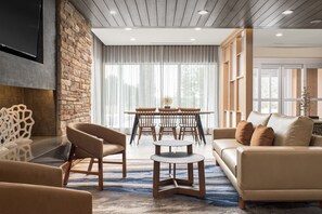 Una sala de estar moderna con una pared de acento de piedra, techo de madera, un sofá, una mesa de centro y un comedor con sillas y una mesa.