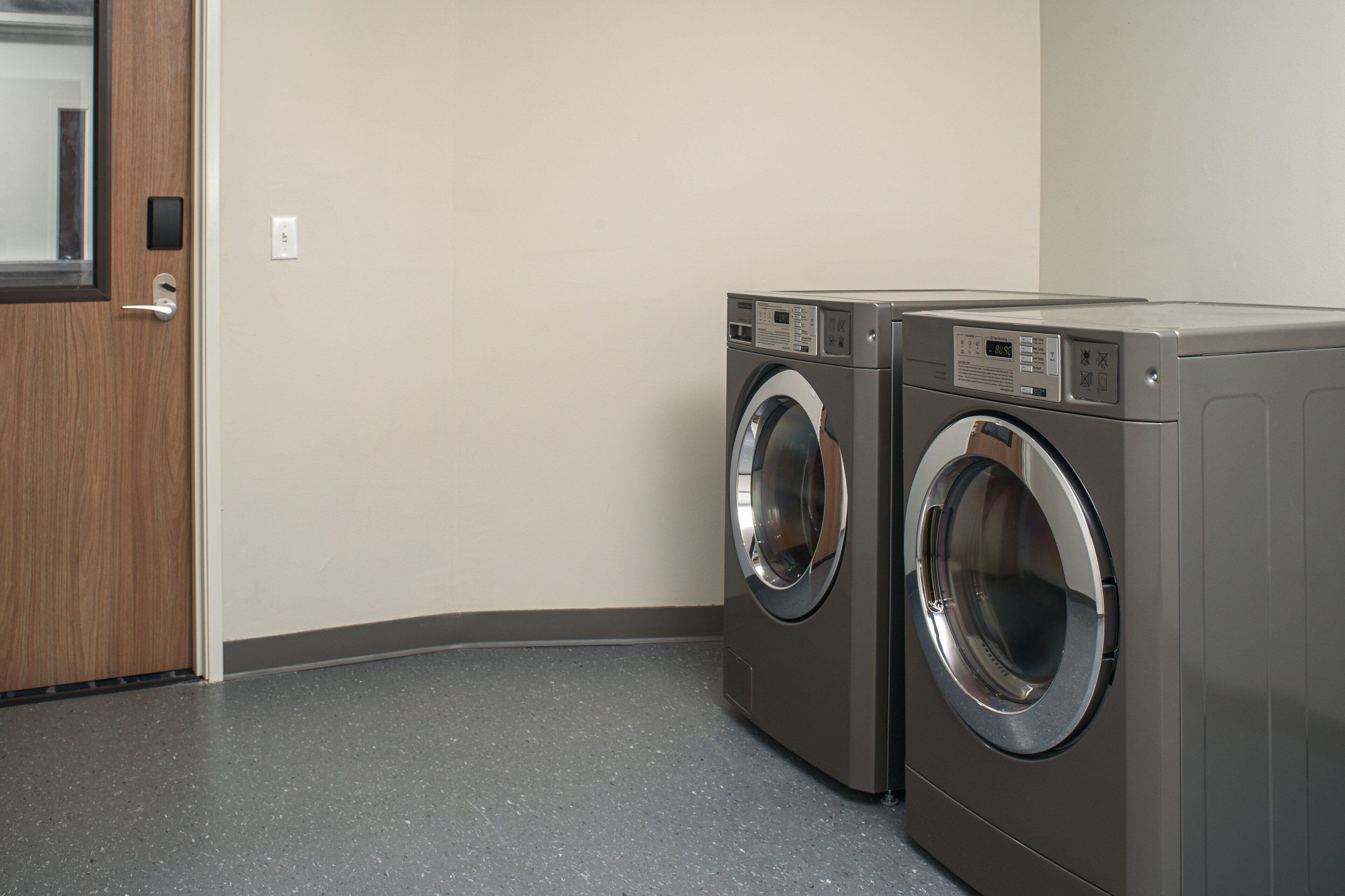 A laundry room with two front-loading washing machines, a wooden door, and a plain wall.