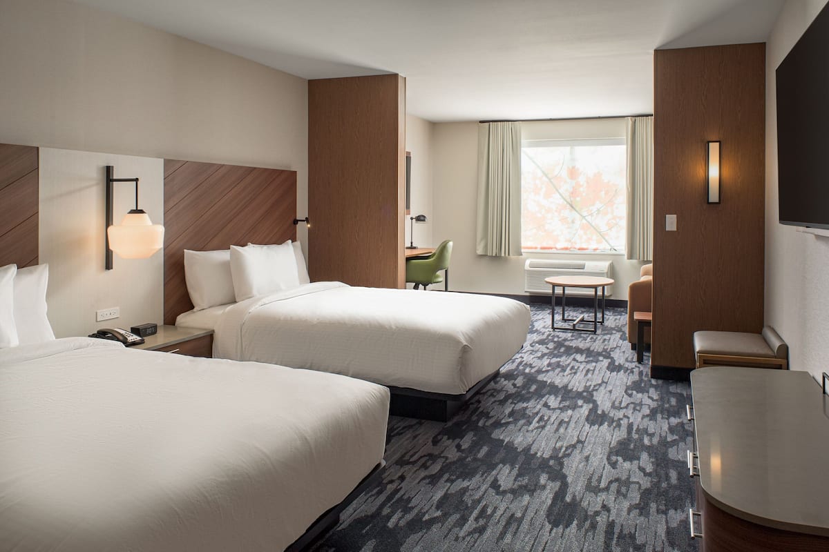 A hotel room with two beds, a desk, a chair, a small table, and a TV.