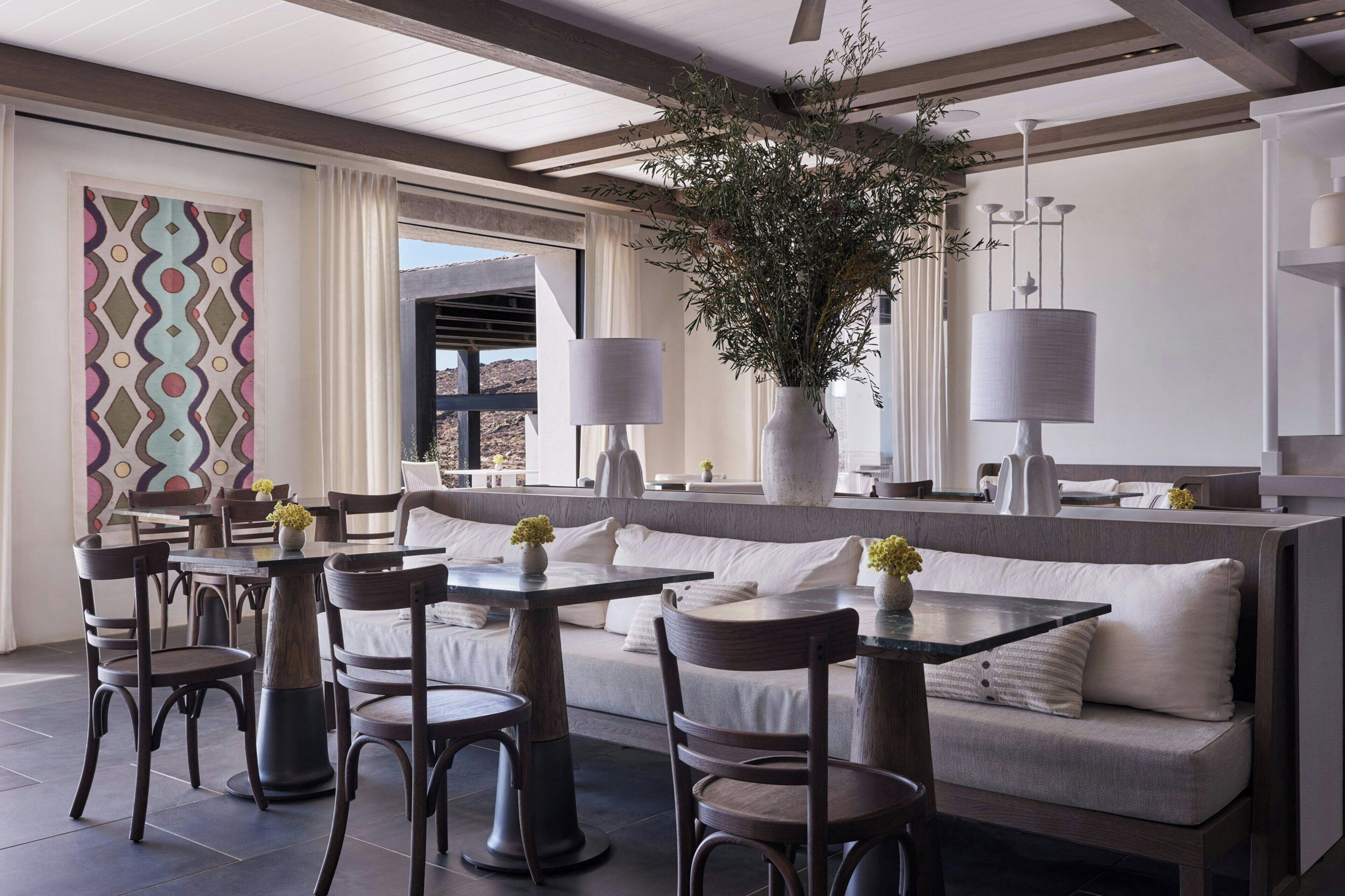A modern dining area with a long table and chairs, a sofa, and a large vase with greenery.