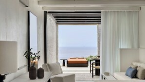 A modern hotel room with a large bed, a seating area with a view of the sea, and a balcony with a table and chairs. - Odera, Tinos, Autograph Collection (Tinos)