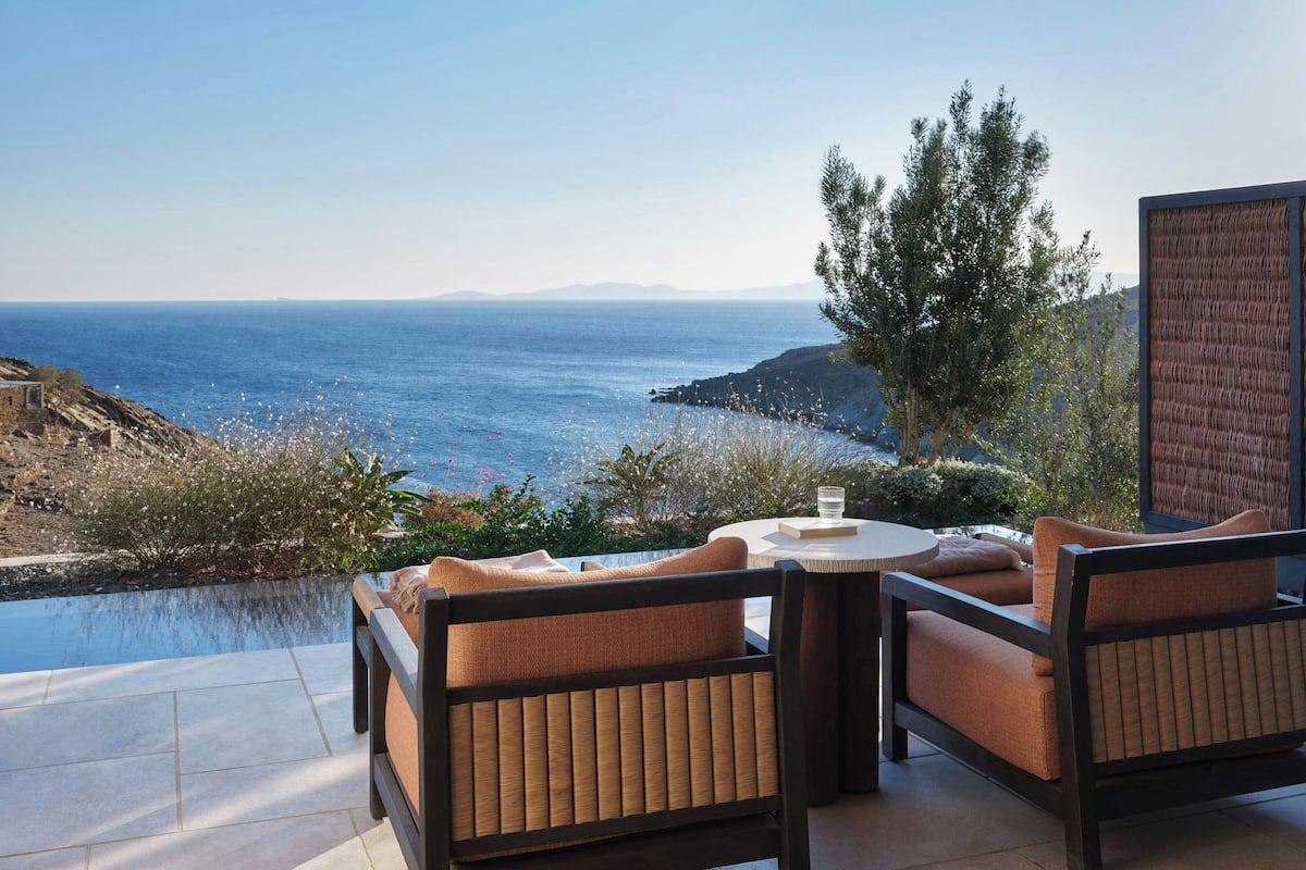 An outdoor seating area with a view of the sea, a pool, and a mountainous landscape.