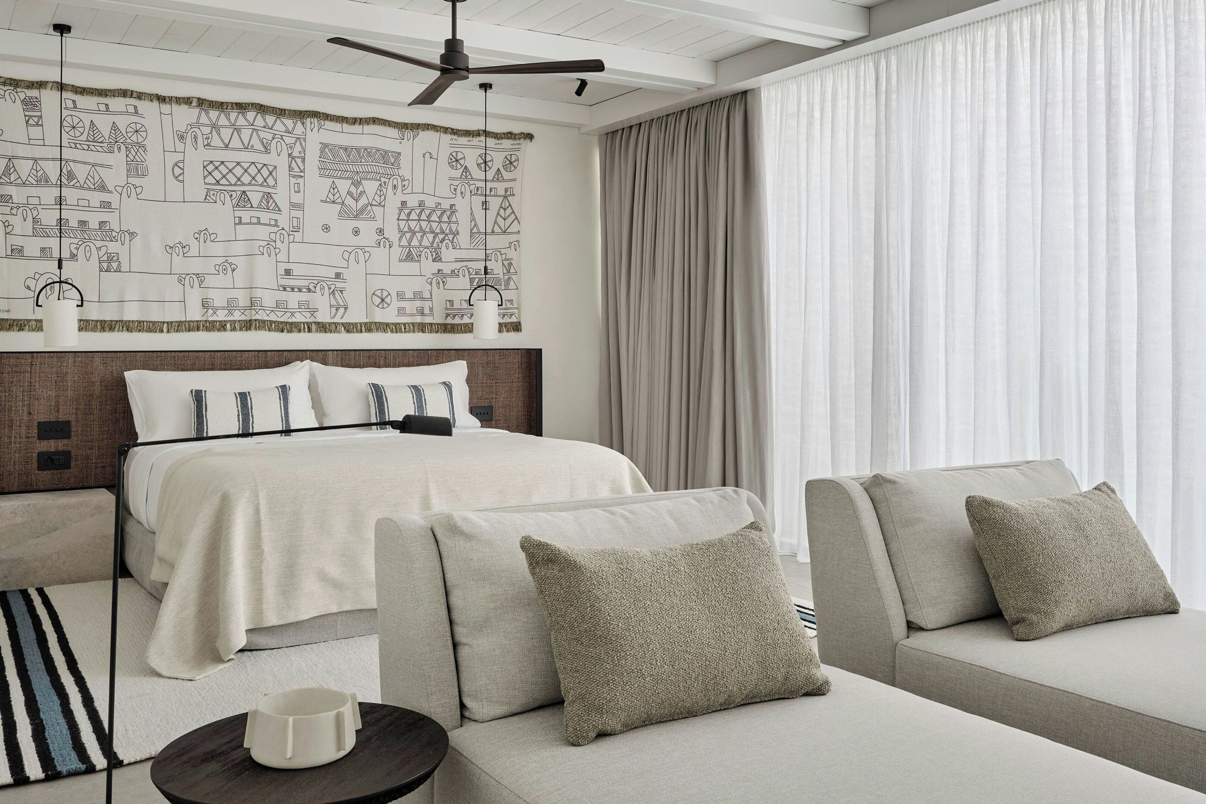 A modern hotel room with a large bed, a sofa, a small table, and a ceiling fan.