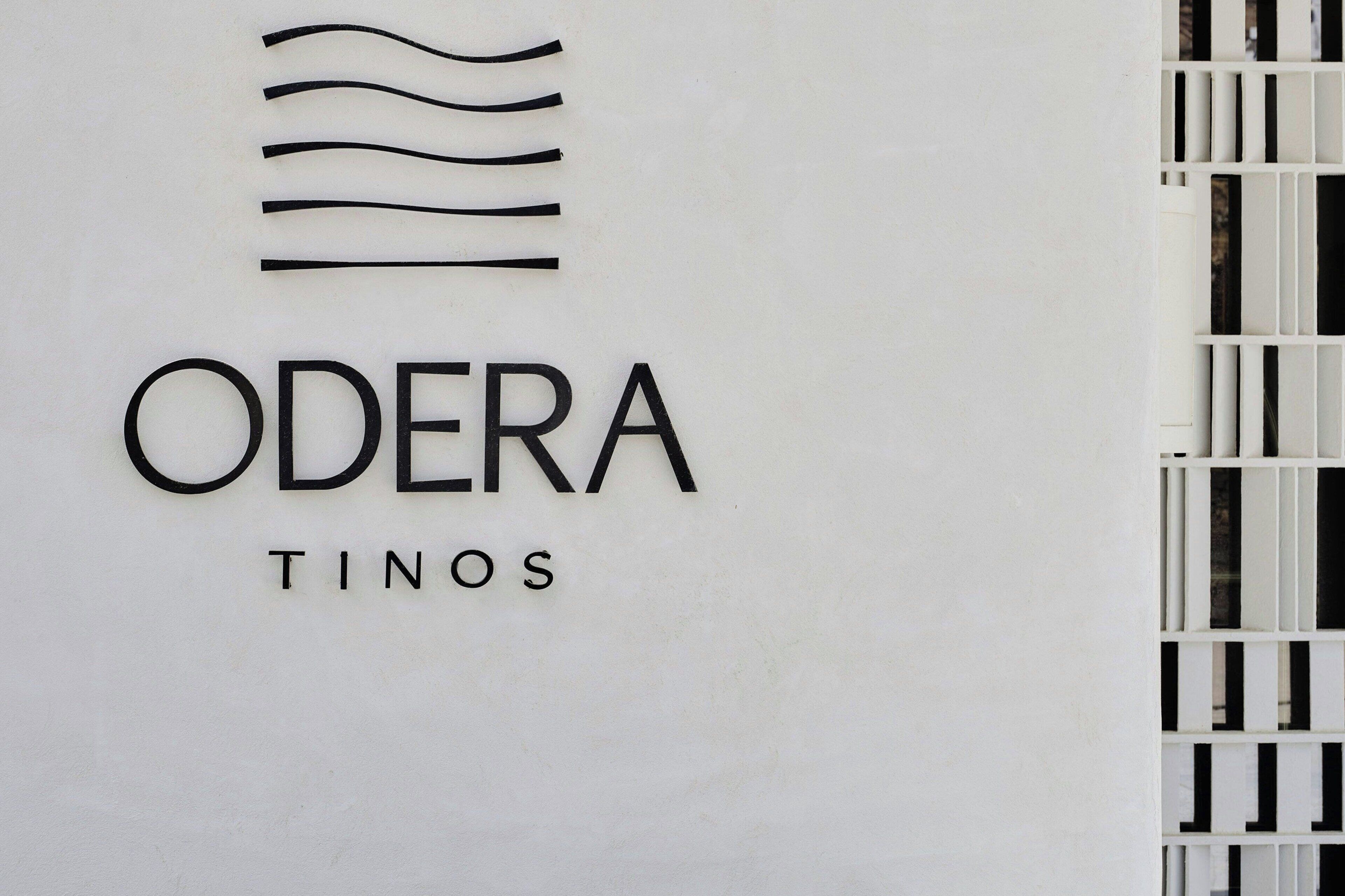 A sign with the text "ODERA TINOS" and a stylized wave design above the text.