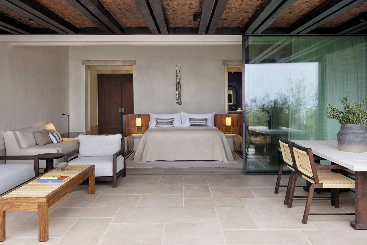 A modern bedroom with a large bed, a sofa, a dining table, and a potted plant.