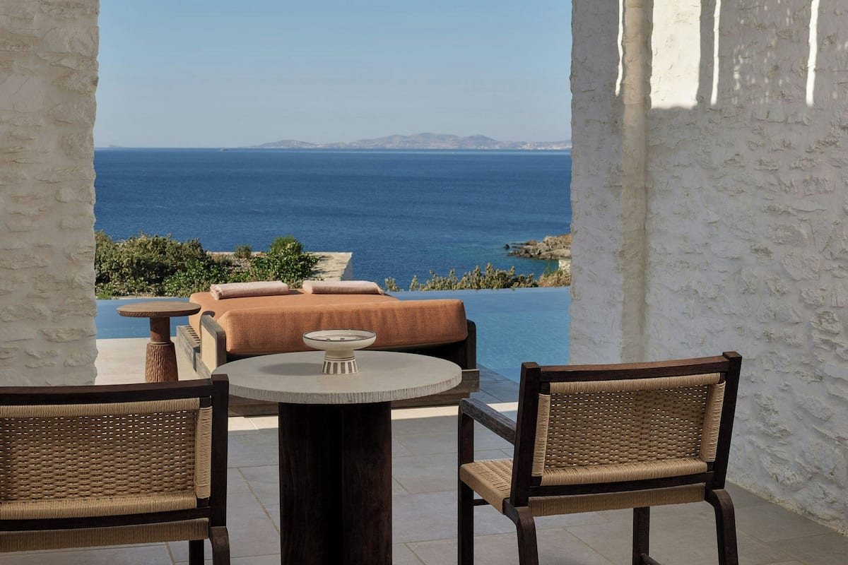 A terrace with wicker furniture, a round table, and a view of the sea.