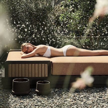 A person lying on a massage table outdoors with a garden in the background.