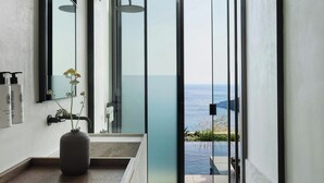 A modern bathroom with a large mirror, a vase with flowers, and a view of the ocean. - Odera, Tinos, Autograph Collection (Tinos)