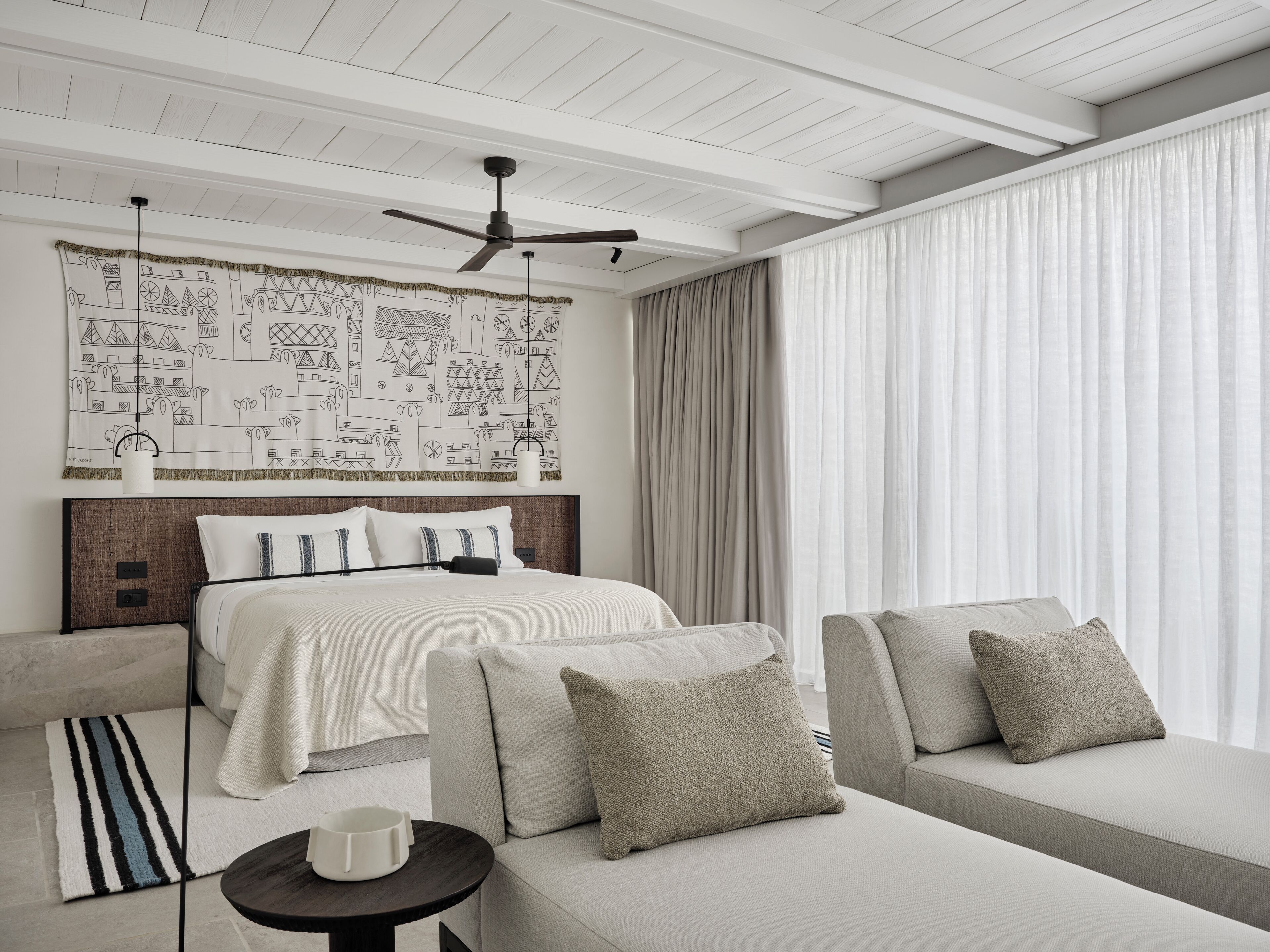 Quarto de hotel moderno com cama, sofá e uma grande janela com cortinas.