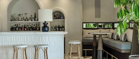 A bar area with a white counter, shelves of liquor bottles, and two stools.