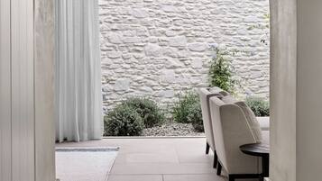 A corridor leading to a patio area with stone walls, a white curtain, and a seating arrangement.